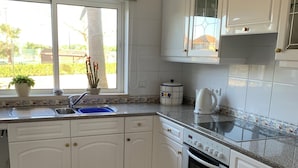 A kitchen with white cabinets, a built-in oven, a sink, and a window with a view of greenery outside.