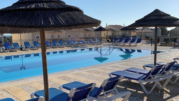 A pool area with lounge chairs and thatched umbrellas.