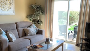 A living room with a sofa, a coffee table, a potted plant, and a sliding glass door leading to an outdoor area.