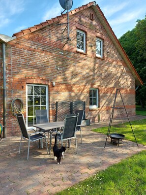 Une maison en briques avec un patio, une antenne parabolique, une table avec des chaises et un chat.