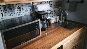 Cocina con microondas, cafetera y lavabo. Se ven armarios de madera y placas de matrícula de Texas.