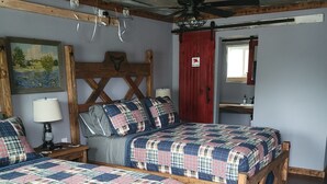 Un dormitorio rústico con dos camas de madera, un ventilador de techo, una puerta roja y un cuadro en la pared.