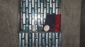 Un baño con pared de azulejos y un estante con artículos de tocador.