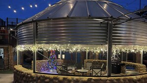 Een overdekt terras met stenen muren, een kerstboom en lichtslingers.