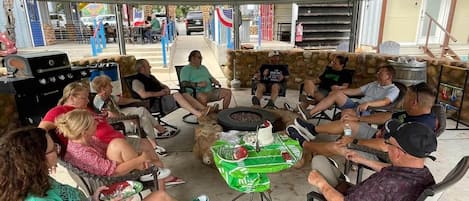 En grupp människor sitter runt ett bord med en tårta under ett takförsett utomhusområde med ett tak av metall.