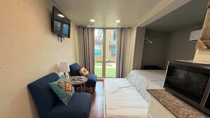 Een compacte hotelkamer met een bed, een bank, een televisie en een klein tafeltje.