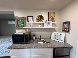 Een kleine kitchenette met een magnetron, koffiezetapparaat en een klein spoelbakje.
