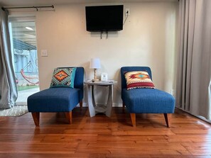 A room with two blue armchairs, a small table with a lamp, and a mounted TV on the wall. - PPI Native American Theme suite-Slps 4 w/Gazebo (Medicine Park)