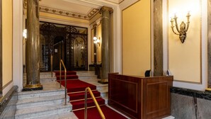 A grand staircase with red carpet and gold railings leading to a wooden reception desk.