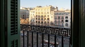 A view from a balcony with a geometric railing, overlooking a street with buildings and a parked car.