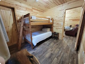 Una habitación de cabaña de madera con literas, una mesita pequeña y un sofá.