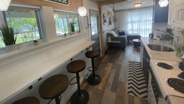 A kitchen with a white stove, a sink, and a bar area with stools. There are potted plants on the windowsill and a sign that reads "BEACH HOUSE". - Cedar Point, Sports Force, Kalahari Near Cottage. Boat Parking ez Walk to Beach! (Huron)