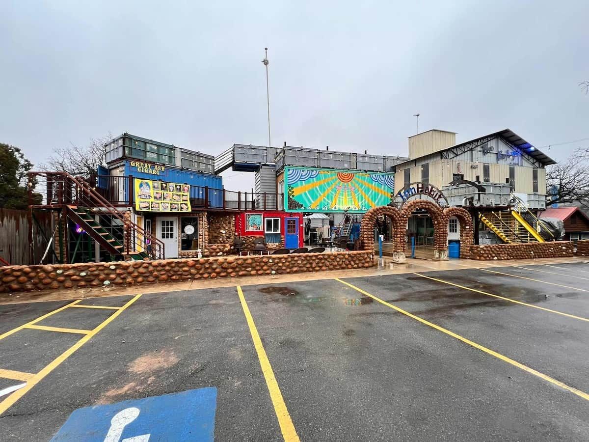 Un estacionamiento con un espacio reservado para discapacitados, un edificio con un mural colorido, y un letrero que dice 'Green Ash Cigar Coasters'.