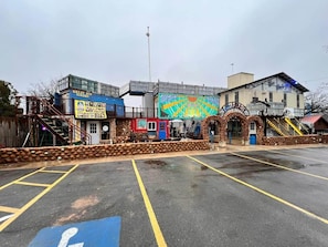 A parking lot with a handicapped parking space, a building with a colorful mural, and a sign for 'Green Ash Cigar Coasters.'