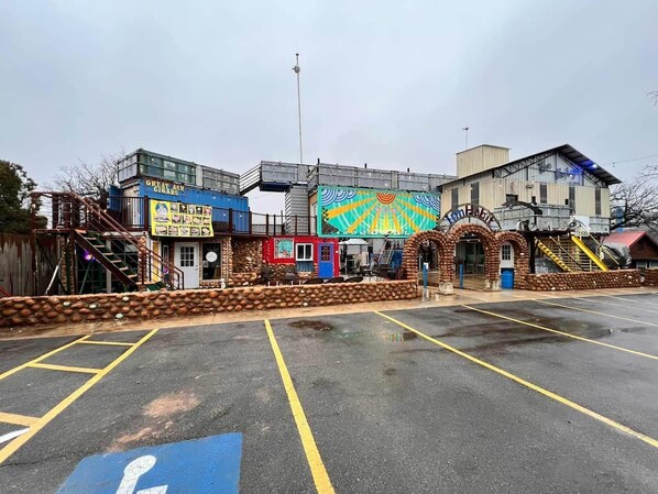 Un estacionamiento con un espacio reservado para discapacitados, un edificio con un mural colorido, y un letrero que dice 'Green Ash Cigar Coasters'.
