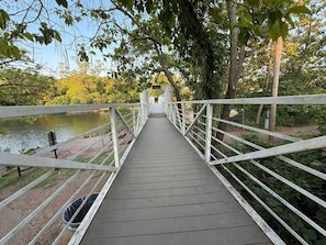 Un puente peatonal de madera con barandillas blancas que cruza un cuerpo de agua, rodeado de árboles.