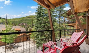 A wooden deck with red Adirondack chairs and a view of a mountainous area.