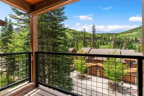 A balcony with a view of a forested mountain area, wooden buildings, and a clear sky.