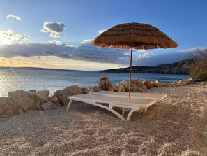 Ein Strand mit einem Reetdachschirm und einer Liege.