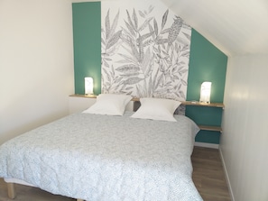 Un lit bien fait, recouvert d’une couvre-lit à motifs, avec deux oreillers blancs, et un mur orné d’un motif floral. On y trouve deux tables de chevet avec des lampes.