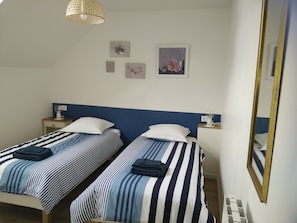 Une chambre double avec deux lits, une table de chevet avec une lampe, une horloge murale et des œuvres d’art encadrées.