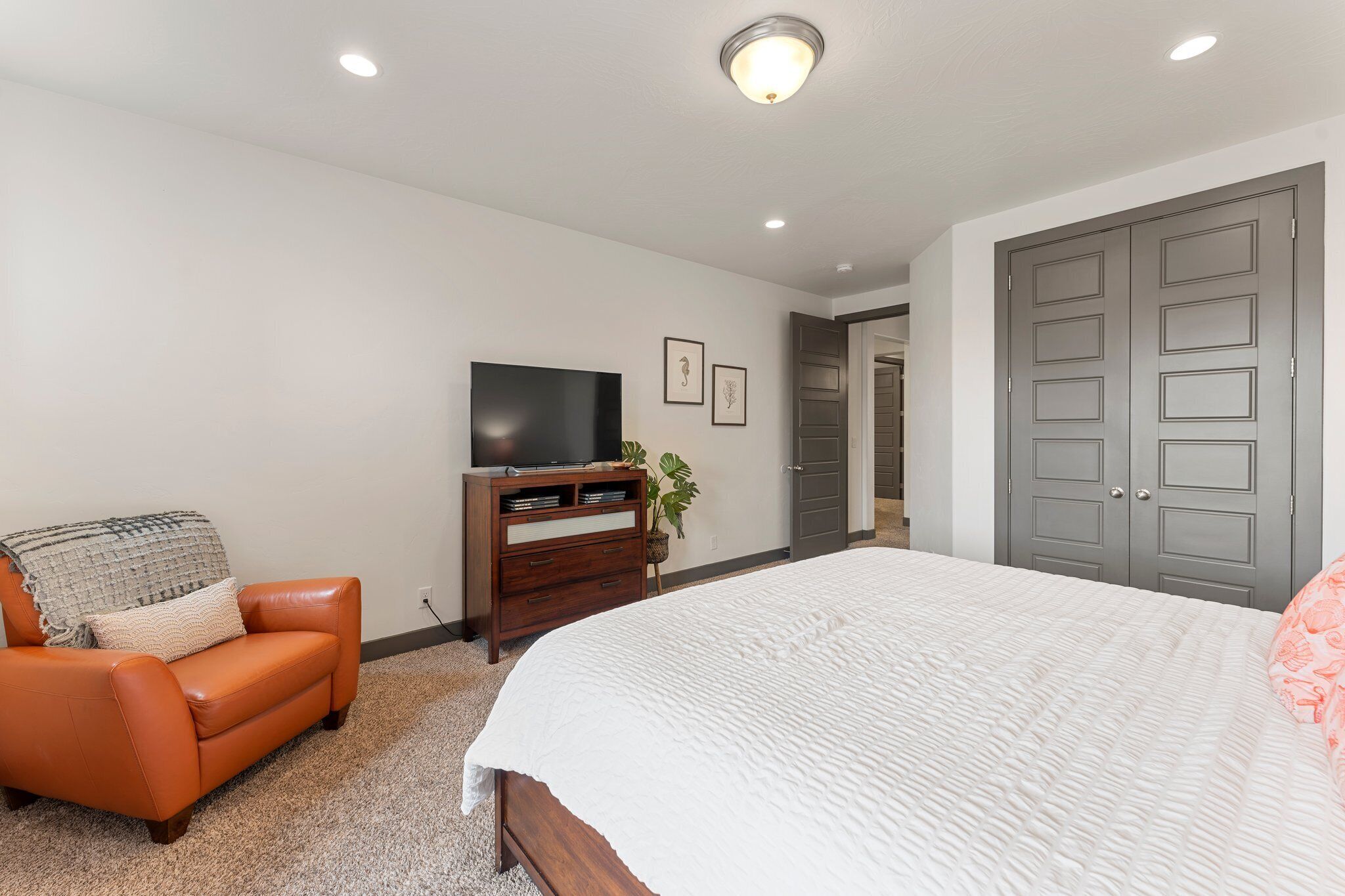 A bedroom with a bed, a sofa, a TV, a dresser, and a closet.