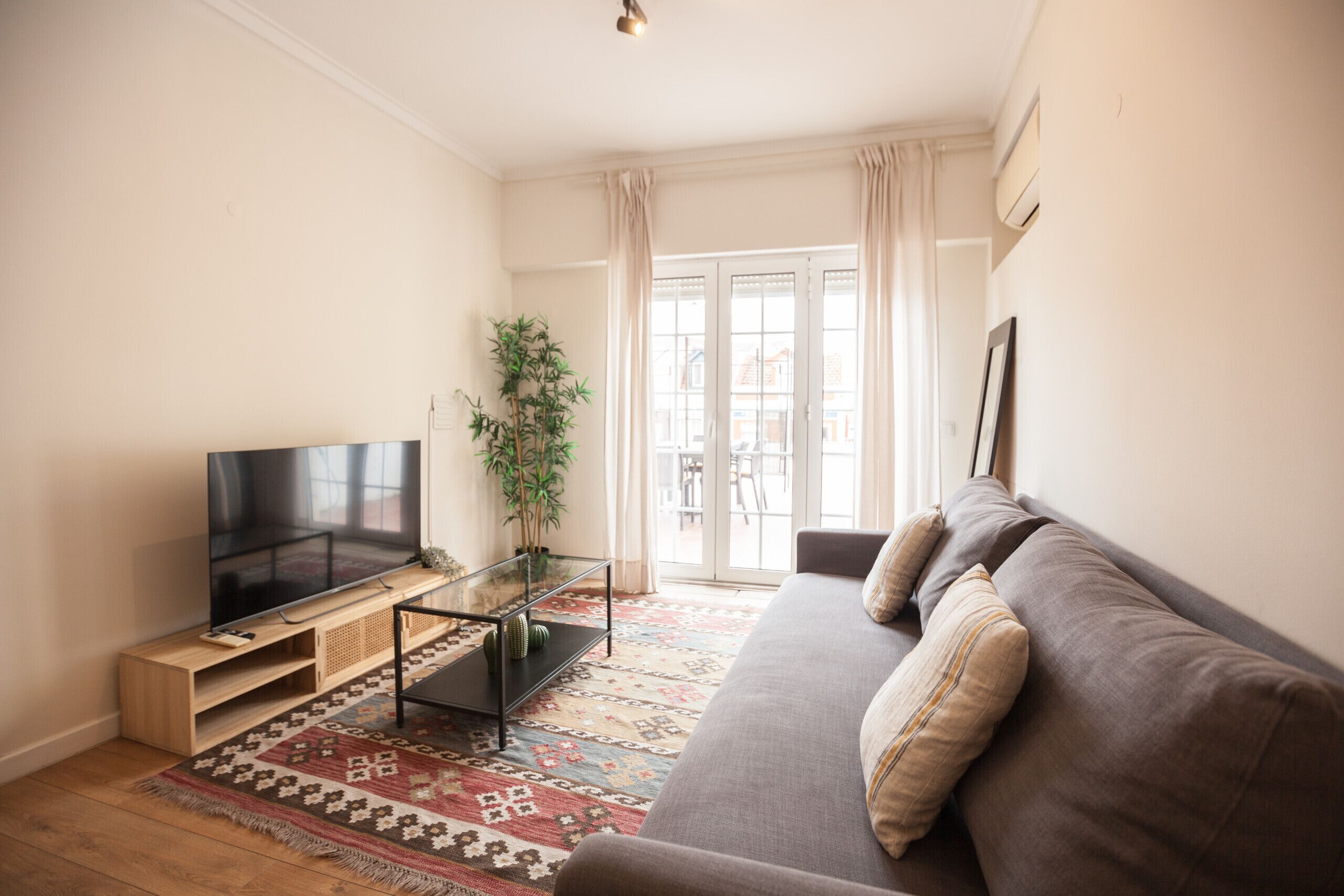 A living room with a flat-screen TV, a sofa, a glass coffee table, and a patterned rug.
