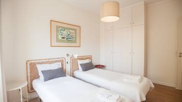 A room with two beds, a small table, a wardrobe, and a hanging light fixture.