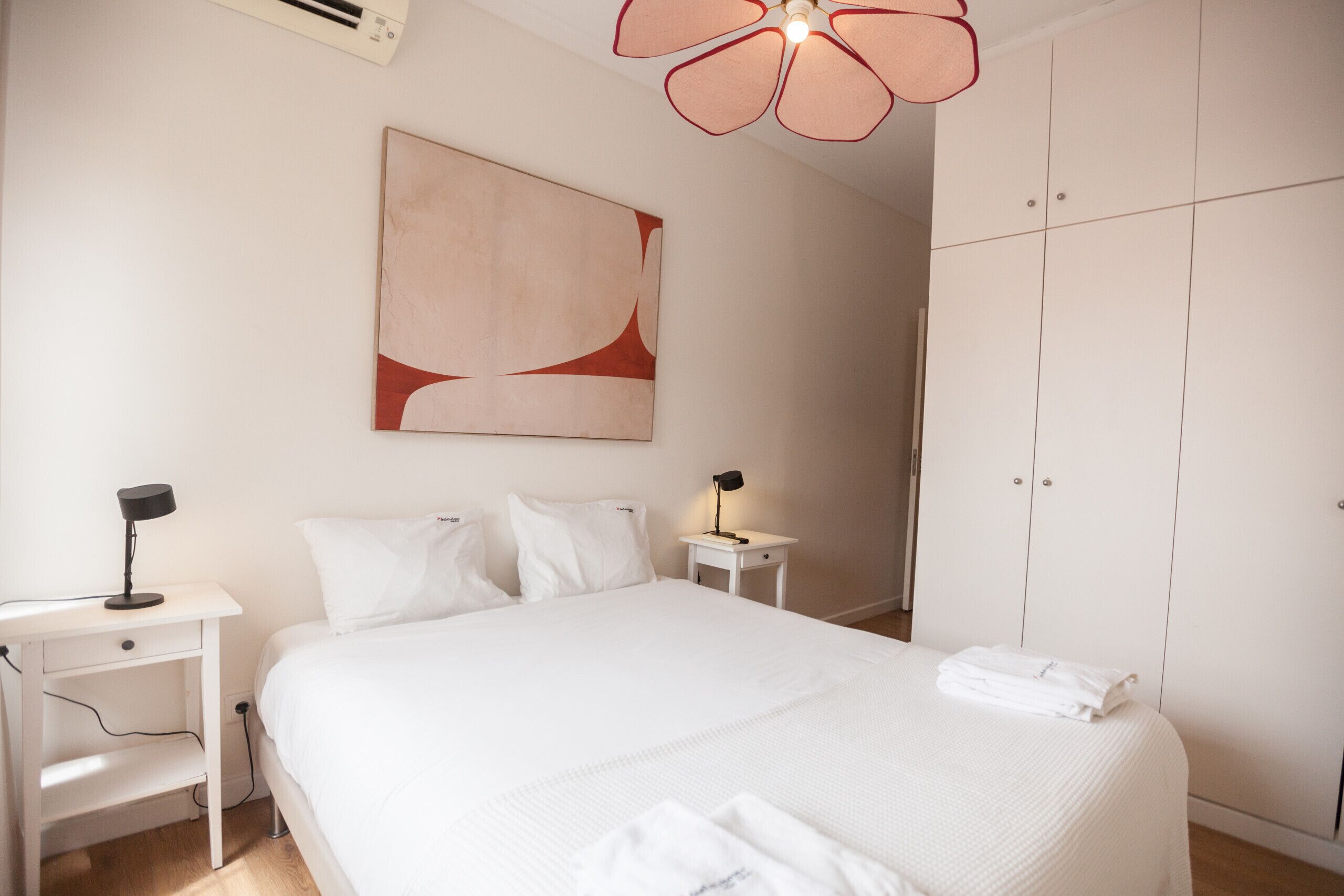 Una habitación de hotel con una cama grande, una mesita de noche con lámpara, un armario y un ventilador de techo.