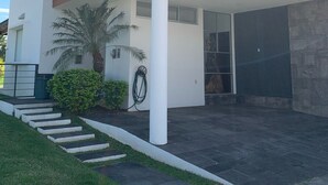 Una casa moderna de dos pisos con techo plano, ventanas grandes y un patio cubierto.