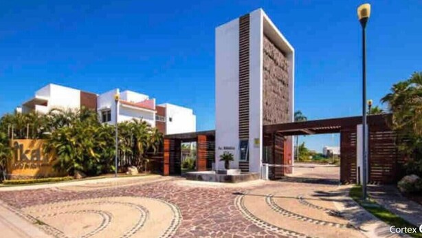 Un edificio moderno con una torre central, una zona de acceso pavimentada y áreas verdes circundantes.