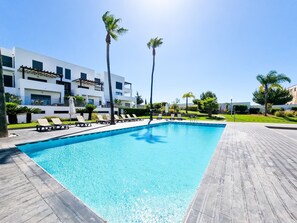 A swimming pool with lounge chairs and palm trees, surrounded by modern buildings.