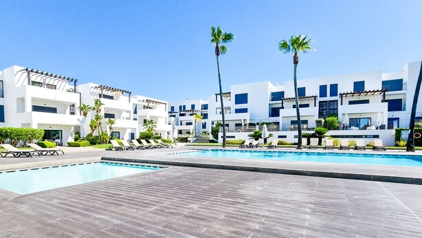 Et moderne hotel med swimmingpool, liggestole og palmer.