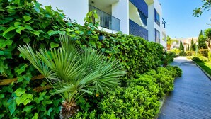 En moderne bygning med et overdækket gangareal, omgivet af frodig vegetation og forskellige planter.