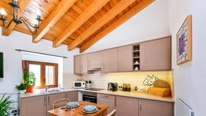 Une cuisine avec des poutres en bois, une table à manger avec des chaises et une fenêtre avec des stores.
