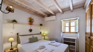 Une chambre à coucher comprenant un lit, des tables de chevet, une fenêtre, une étagère avec des plantes et un climatiseur fixé au mur.