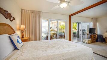 A hotel room with a large bed, a ceiling fan, a TV, and a balcony with outdoor furniture.