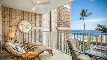A balcony with a view of the ocean, furnished with lounge chairs and a table.