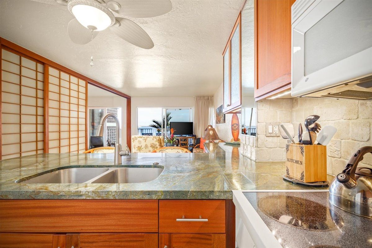 A kitchen with wooden cabinets, a granite countertop, a sink, and a kettle.