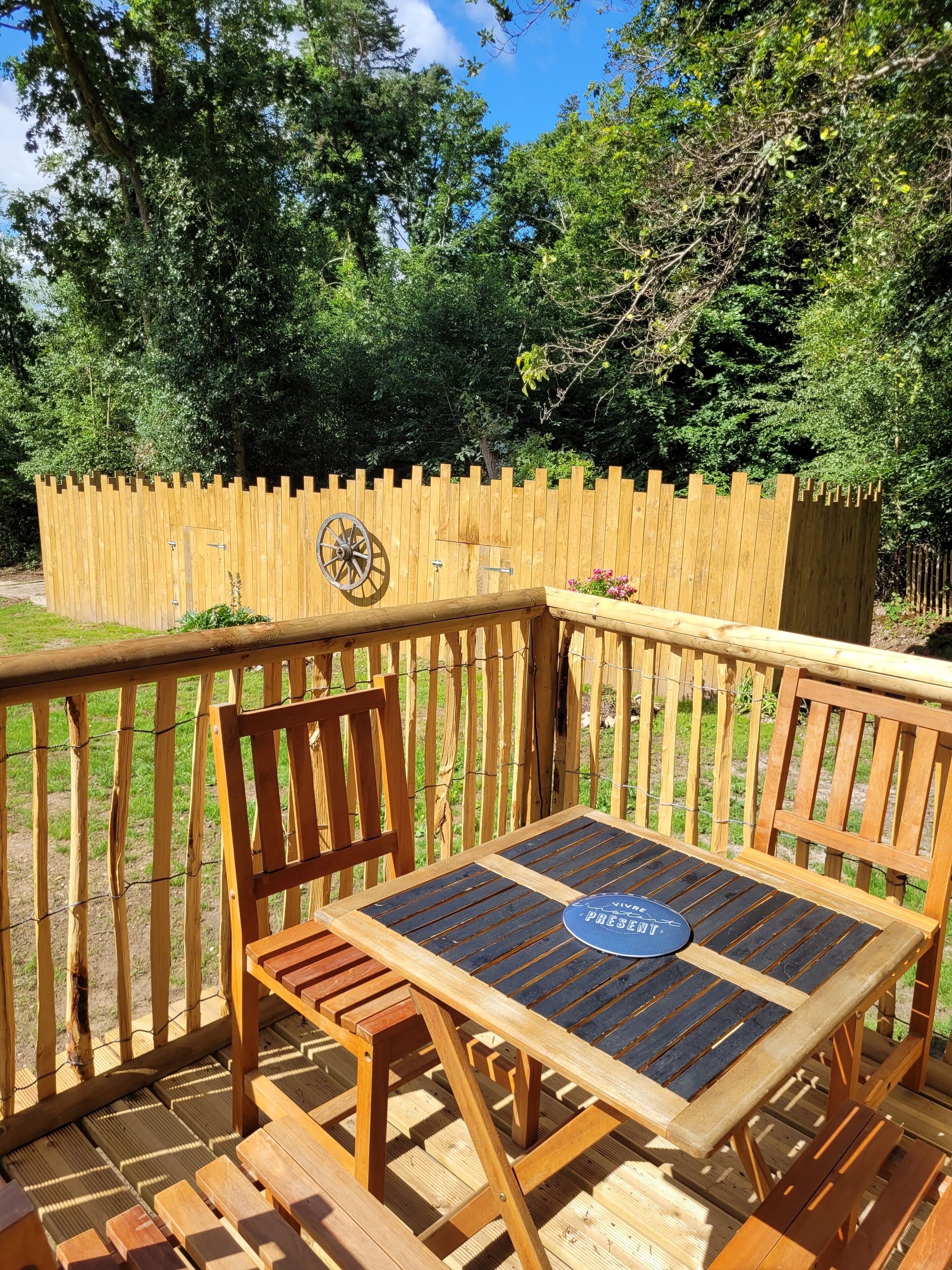 Una terraza de madera con una mesa y sillas, rodeada por una valla de madera y vegetación.