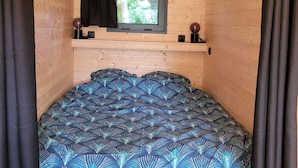 A cozy cabin room with a bed, a window, and a shelf with a globe and a speaker. - Roulotte Escapade nature in Morainville (Morainville-Jouveaux)