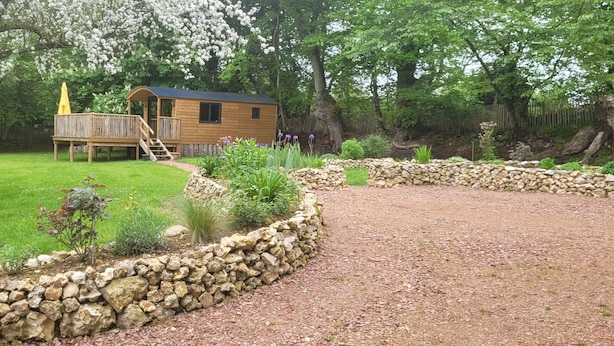 A wooden cabin with a deck, surrounded by a stone wall and a gravel path. - Roulotte Escapade nature in Morainville (Morainville-Jouveaux)