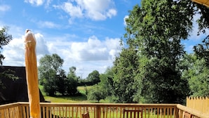 A wooden deck with a table and chairs, surrounded by a wooden fence, overlooking a green landscape. - Roulotte Escapade nature in Morainville (Morainville-Jouveaux)