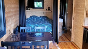 A compact wooden cabin with a dining area, a bed with a patterned bedspread, and a television mounted on the wall. - Roulotte Escapade nature in Morainville (Morainville-Jouveaux)