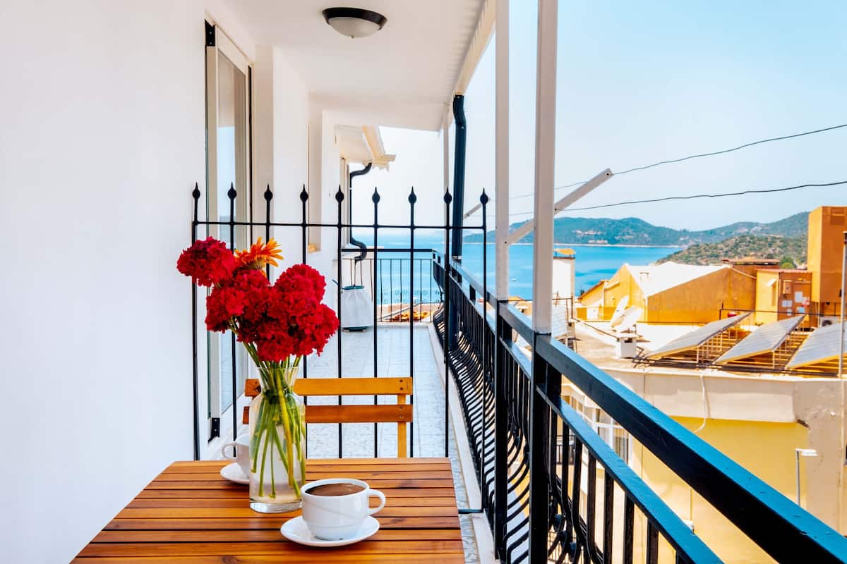 Uma varanda com uma mesa de madeira, uma xícara branca e um vaso de flores vermelhas.