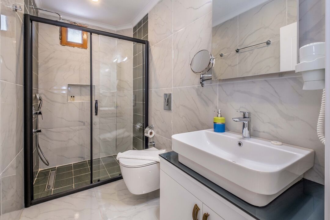 A modern bathroom with a glass-enclosed shower, a white sink, and a toilet.