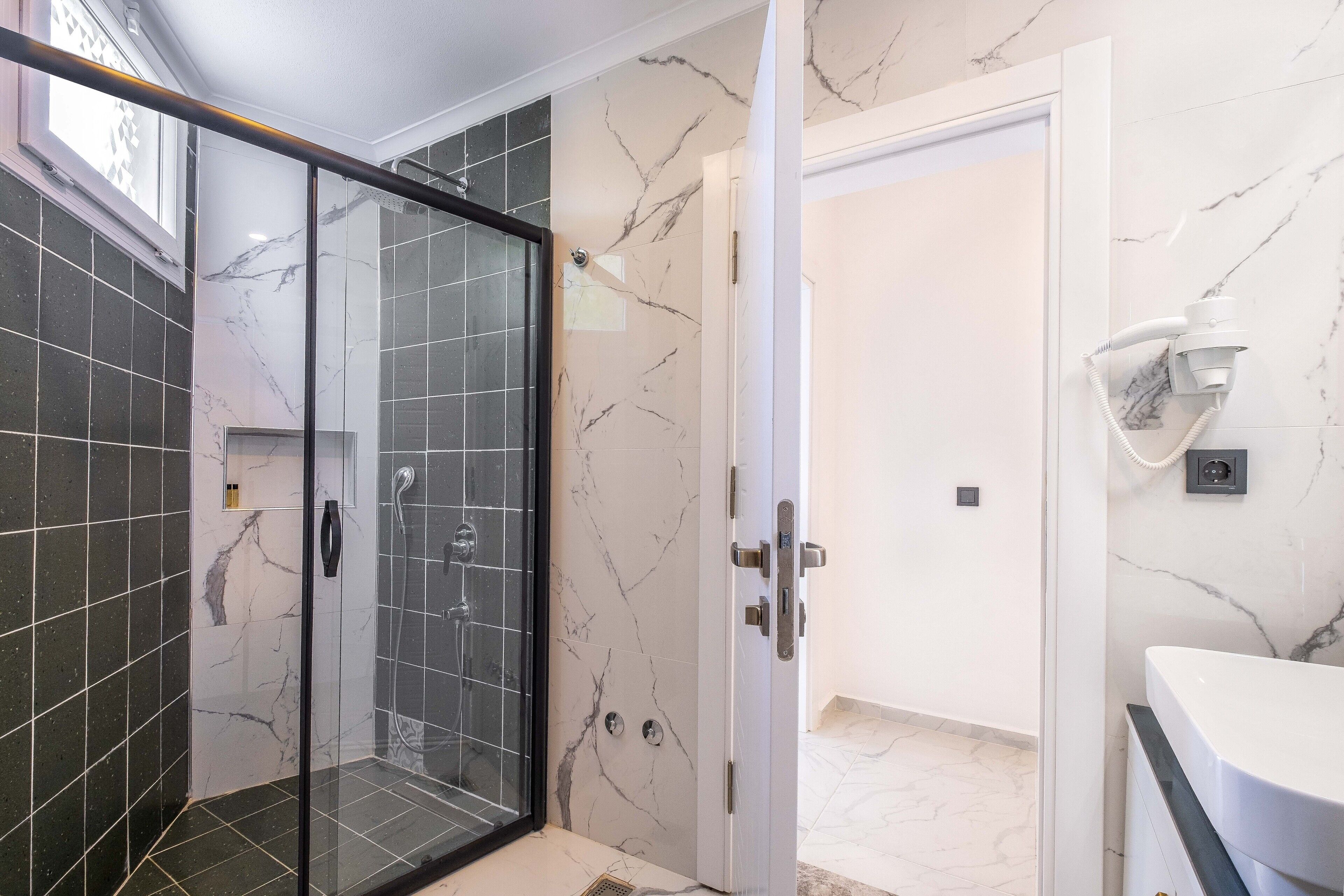 Un baño moderno con ducha de mampara de vidrio, lavamanos blanco y paredes de mármol.