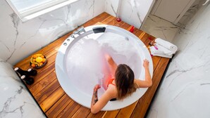 Una mujer descansando en un jacuzzi con piso de madera y paredes de mármol.