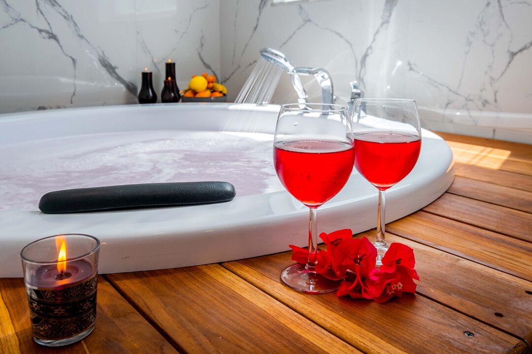 Un baño con lavamanos de mármol, una bañera y dos vasos de bebida roja.