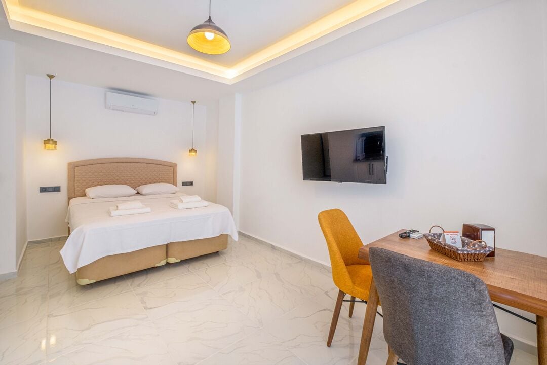 Habitación de hotel con cama, televisor montado en la pared, mesa de comedor con una silla y lámpara de techo.